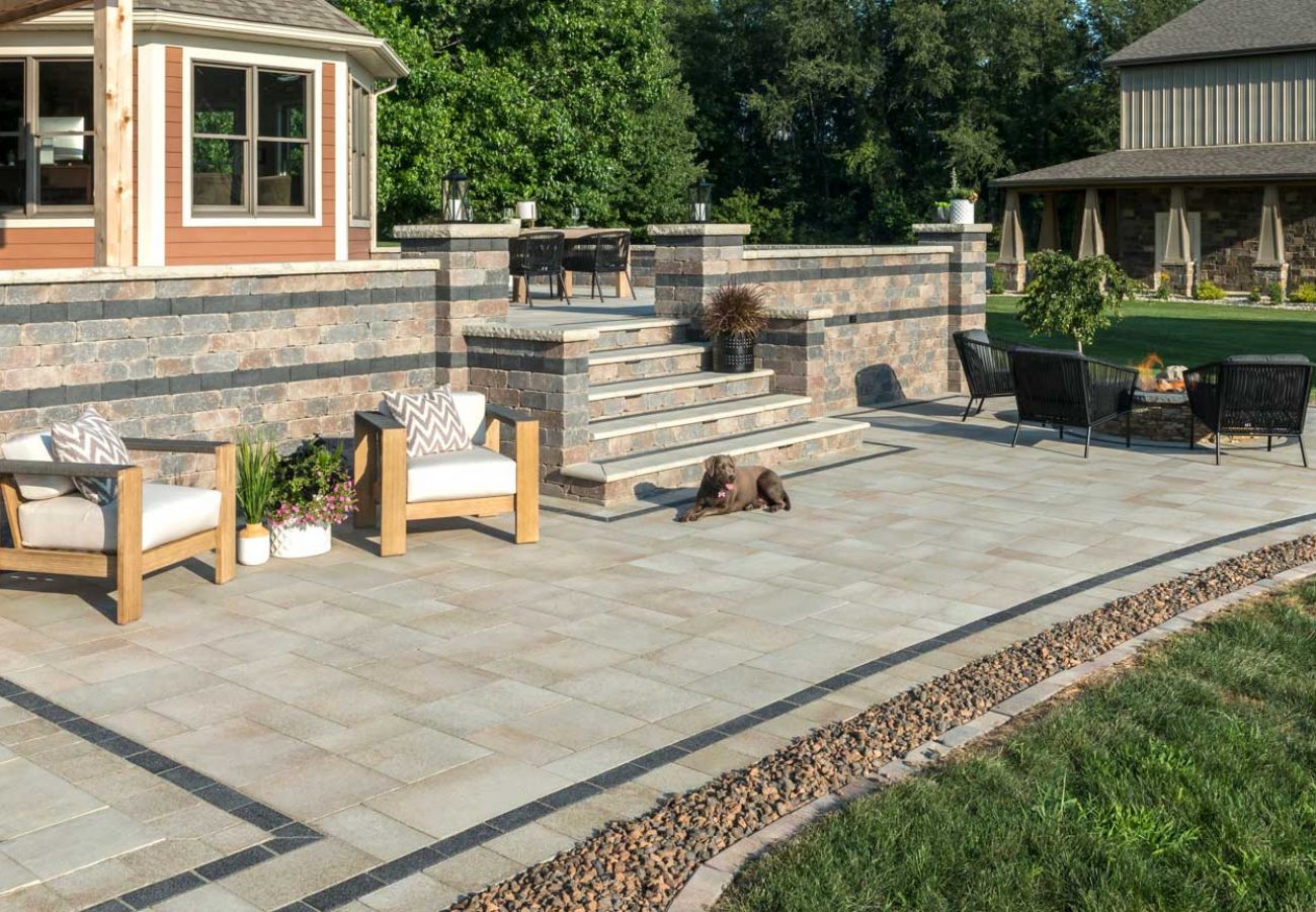 Multi-level paver patio with stone steps, outdoor seating, and retaining wall accents in a landscaped yard.