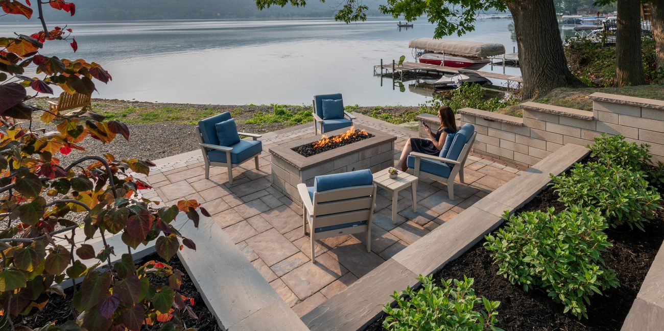 Professionally designed patio oasis with fire pit, lake views, inviting seating, and attractive surrounding greenery.