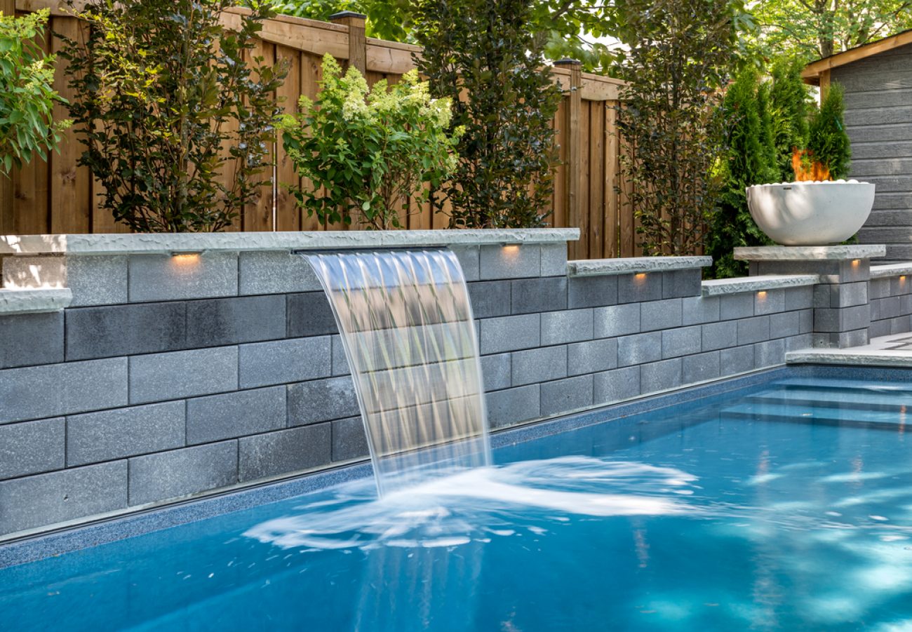Modern backyard pool with elegant waterfall feature, ambient lighting, and lush greenery for tranquil outdoor living.