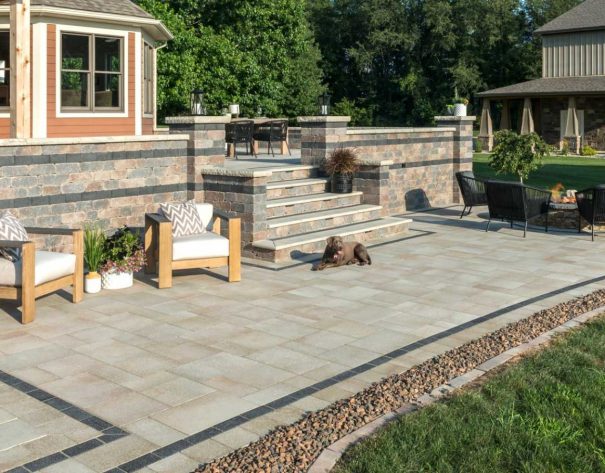 Multi-level paver patio with stone steps, outdoor seating, and retaining wall accents in a landscaped yard.